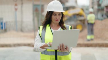 Young beautiful hispanic woman architect using laptop at street