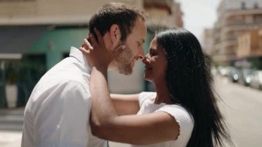 Man and woman interracial couple hugging each other and kissing at street