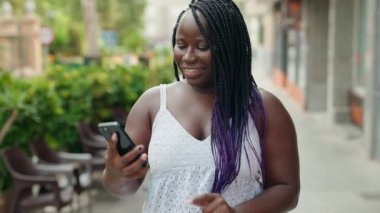 Afro-Amerikalı bir kadın kahve dükkanının terasında kendinden emin bir şekilde selfie çekiyor.