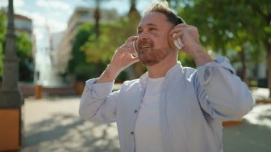 Parkta müzik dinlerken kendinden emin gülümseyen beyaz bir genç.