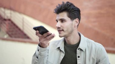 Young hispanic man smiling confident sending voice message by smartphone at street
