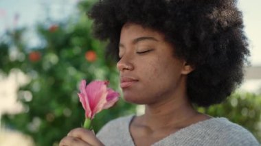 African american woman smiling confident smelling flower at park