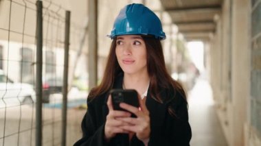 Young hispanic woman architect using smartphone at street