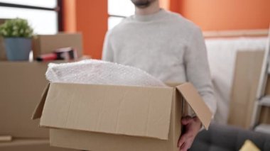 Genç İspanyol adam yeni evinde kendine güvenen bir paket tutuyor.