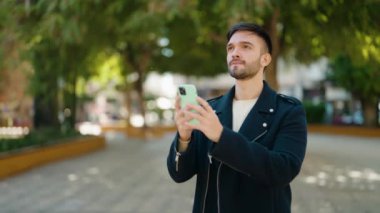 Genç İspanyol adam gülümsüyor. Parktaki akıllı telefonun yanında özçekim yapıyor.