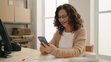 Middle age woman ecommerce business worker using smartphone at office