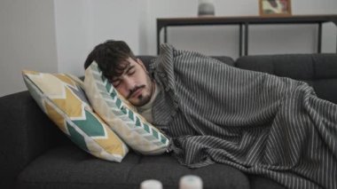Genç İspanyol adam kanepede hasta yatıyordu. Evdeki masada peçeteler ve haplar vardı.