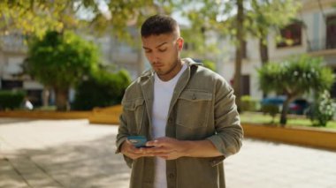 Young hispanic man using smartphone at park