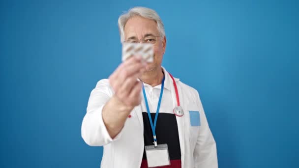 中年男子与灰发医生持有药丸与孤立的蓝色背景 — 图库视频影像
