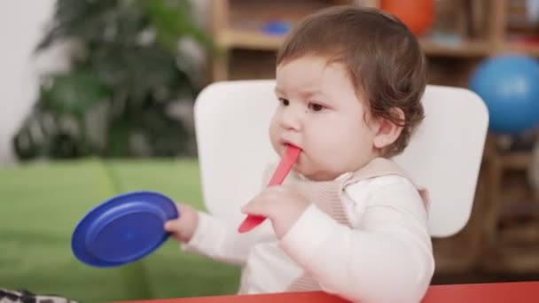 愛らしい幼児座っています上のテーブル吸いプラスチックスプーン保持皿で幼稚園 — ストック動画