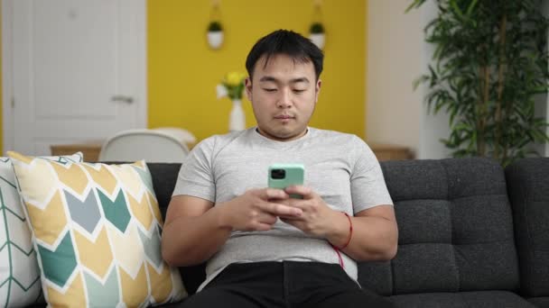 自宅で心配そうな表情のスマートフォンを使っている若い中国人男性 — ストック動画