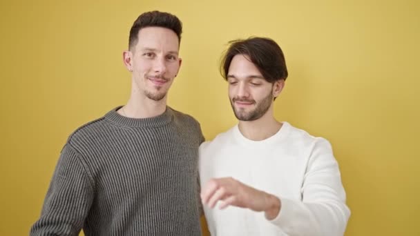 Δύο Άνδρες Ζευγάρι Αγκαλιάζονται Κάνοντας Χειρονομία Καρδιάς Απομονωμένο Κίτρινο Φόντο — Αρχείο Βίντεο
