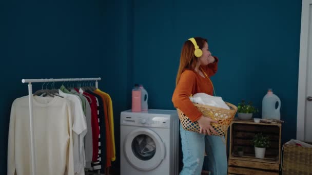 Young Redhead Woman Listening Music Holding Basket Clothes Laundry Room — Vídeo de stock