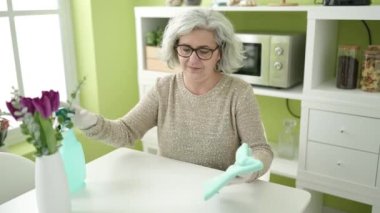 Middle age woman with grey hair cleaning table at home