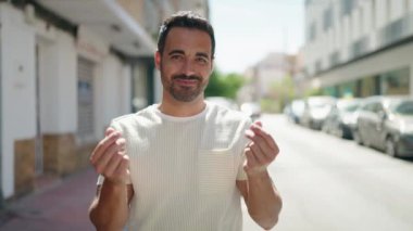 Young hispanic man smiling confident doing spend money gesture at street