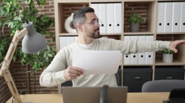 Genç İspanyol iş adamı dizüstü bilgisayarını kullanarak ofiste dans eden belgeleri fırlatıyor.