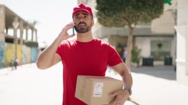 Genç İspanyol teslimatçı elinde paketle caddedeki akıllı telefondan konuşuyor.