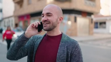 Genç kel adam gülümsüyor. Kendine güveni tam. Akıllı telefondan konuşuyor.