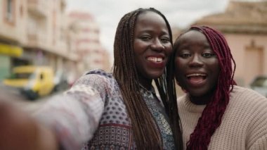 Two african american women smiling confident having video call at street