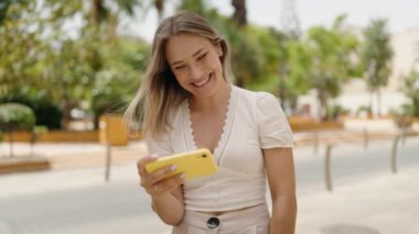 Beyaz kadın gülümsüyor. Sokakta akıllı telefondan videoyu izlerken kendine güveniyor.