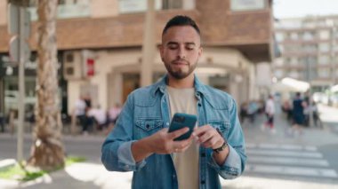 Genç İspanyol adam gülümsüyor. Sokakta akıllı telefonun yanında özçekim yapıyor.