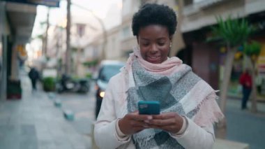 Young african american woman smiling confident using smartphone at street