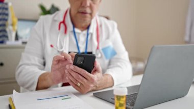 Gri saçlı, orta yaşlı bir adam klinikte çalışan akıllı telefonu kullanıyor.