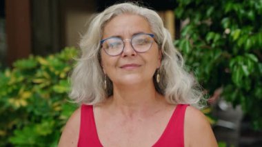 Orta yaşlı, kır saçlı, gülümseyen, kendine güvenen bir kadın.