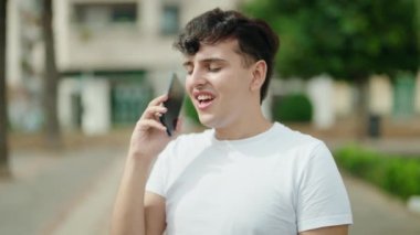 Parkta akıllı telefondan konuşan ikili olmayan bir adam kazanan ifadeyle konuşuyor.