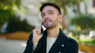 Genç İspanyol adam gülümsüyor. Parktaki akıllı telefondan konuşuyor.