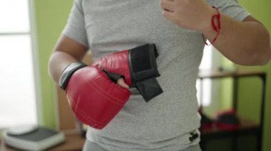 Genç Çinli bir adam spor merkezinde boks eldivenlerini çıkarıyor.