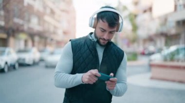 Young hispanic man smiling confident playing video game at street