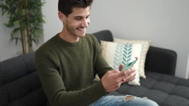 Evdeki kanepede uzanmış akıllı telefon kullanan genç bir İspanyol.