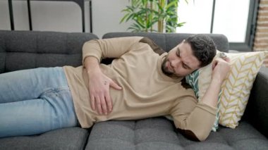 Genç Arap adam mide ağrısı çekiyor. Evdeki kanepede yatıyor.