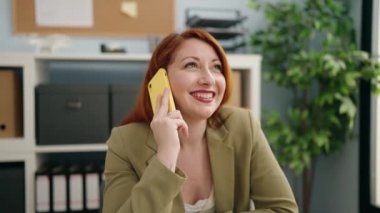 Genç kızıl saçlı iş kadını ofisteki akıllı telefondan konuşuyor.
