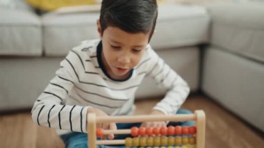 Adorable hispanic boy playing with abacus sitting on floor at home