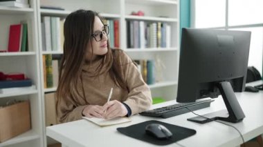 Güzel İspanyol kız öğrenci kütüphanede defter üzerine bilgisayar kullanıyor.