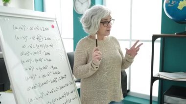 Middle age woman with grey hair teacher teaching maths lesson at university classroom