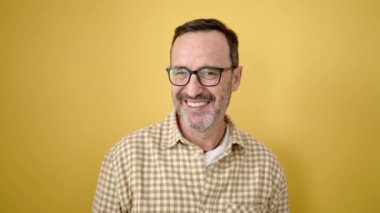 Orta yaşlı bir adam, kendine güvenen, gözlüklü, izole edilmiş sarı arka plan.