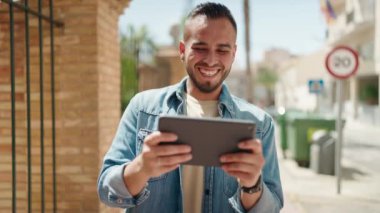 Latin kökenli genç adam gülümsüyor. Touchpad 'de videolar izliyor.