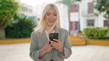 Genç sarışın kadın yönetici parkta akıllı telefon kullanıyor.