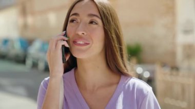 Genç, güzel, İspanyol bir kadın gülümsüyor ve caddede akıllı telefondan konuşuyor.