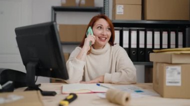 Genç kızıl saçlı kadın iş kadını ofisteki akıllı telefondan konuşuyor.