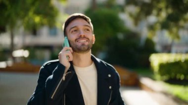 Genç İspanyol adam gülümsüyor. Parktaki akıllı telefondan konuşuyor.
