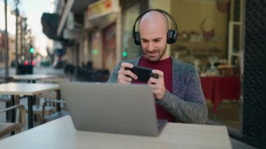 Kafe terasında video oyunu oynarken kendine güvenen kel bir genç adam.
