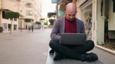 Sokakta dizüstü bilgisayar kullanan kel bir adam.