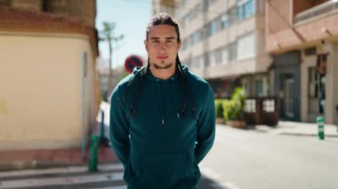 Genç adam kendinden emin gülümsüyor. Kollarını kavuşturup caddede hareketler yapıyor.