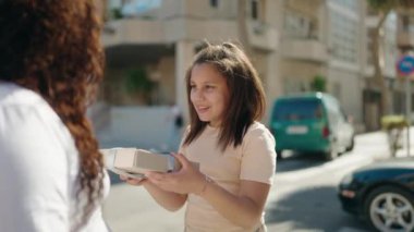 Mother and daughter smiling confident surprise with gift at street