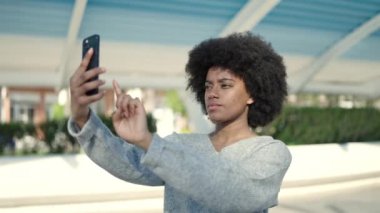 Afro-Amerikalı kadın, parkta akıllı telefonun yanında kendinden emin bir şekilde selfie çekiyor.