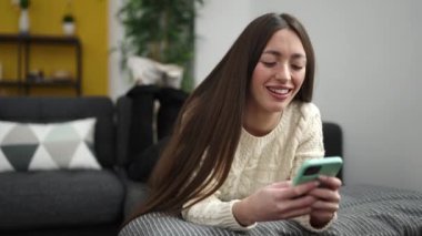 Evdeki kanepede uzanmış akıllı telefon kullanan genç, güzel İspanyol kadın.